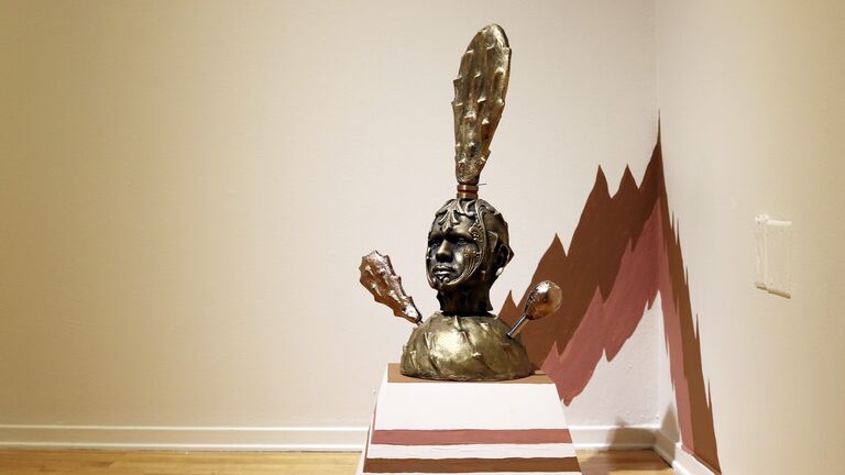 An installation view of a statue of a man's bust with a cactus growing from his scalp. 