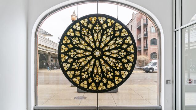 circular stained glass window that is black and green in front of a larger street-facing window in a white room