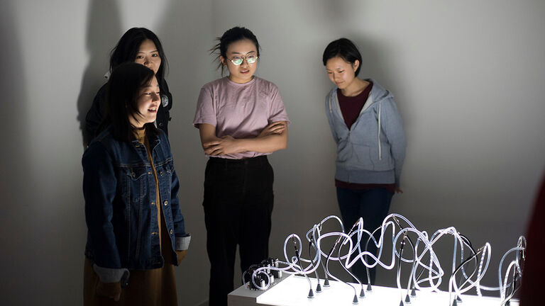 Three students stand around a light installation