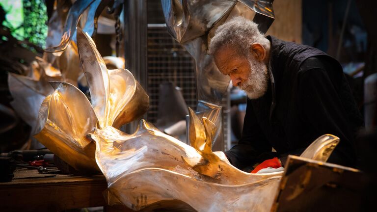 A sculptor works on a metal piece in his studio
