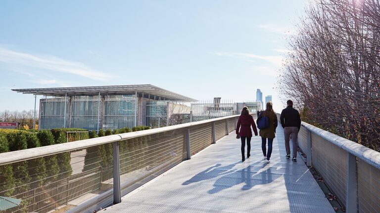 Three people walk across a bridge toward the Art Institute of Chicago.