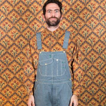 A person in overalls wears a shirt the same pattern as the photo background