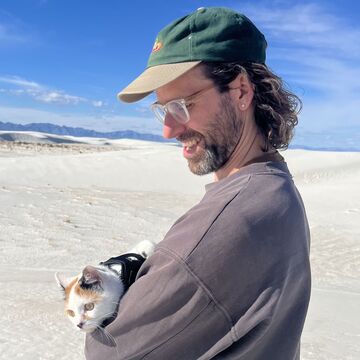 David stands in a desert holding a cat.