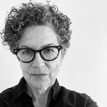 Black and white selfie of an adult person with a medium-fair skin tone, short dark curly hair and glasses.
