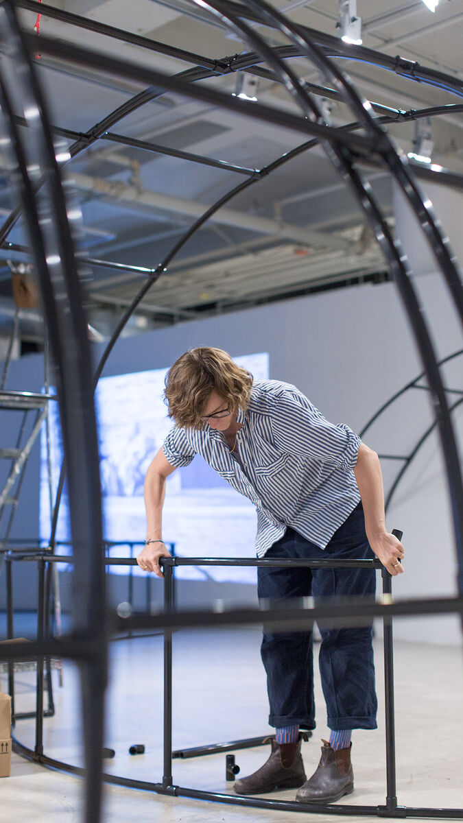 A student installing a large, black metal frame in an open gallery. 