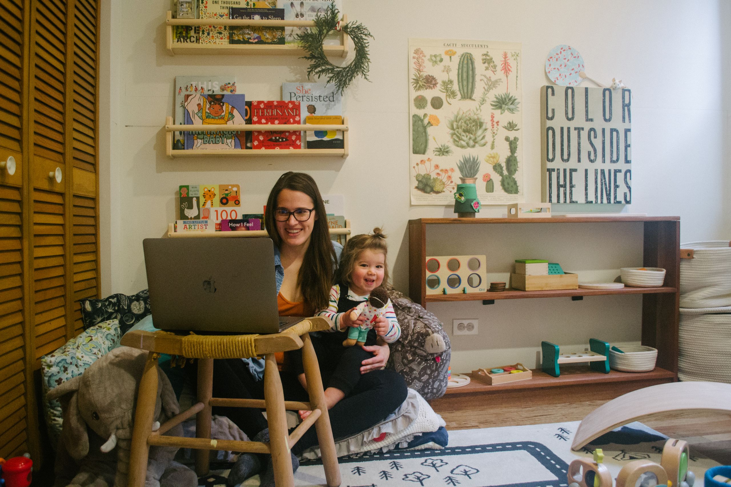 Calderon looking at her laptop while holding her young daughter in her cheerily decorated nursery