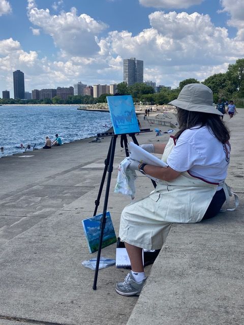 A student paints on a pier in front of Lake Michigan