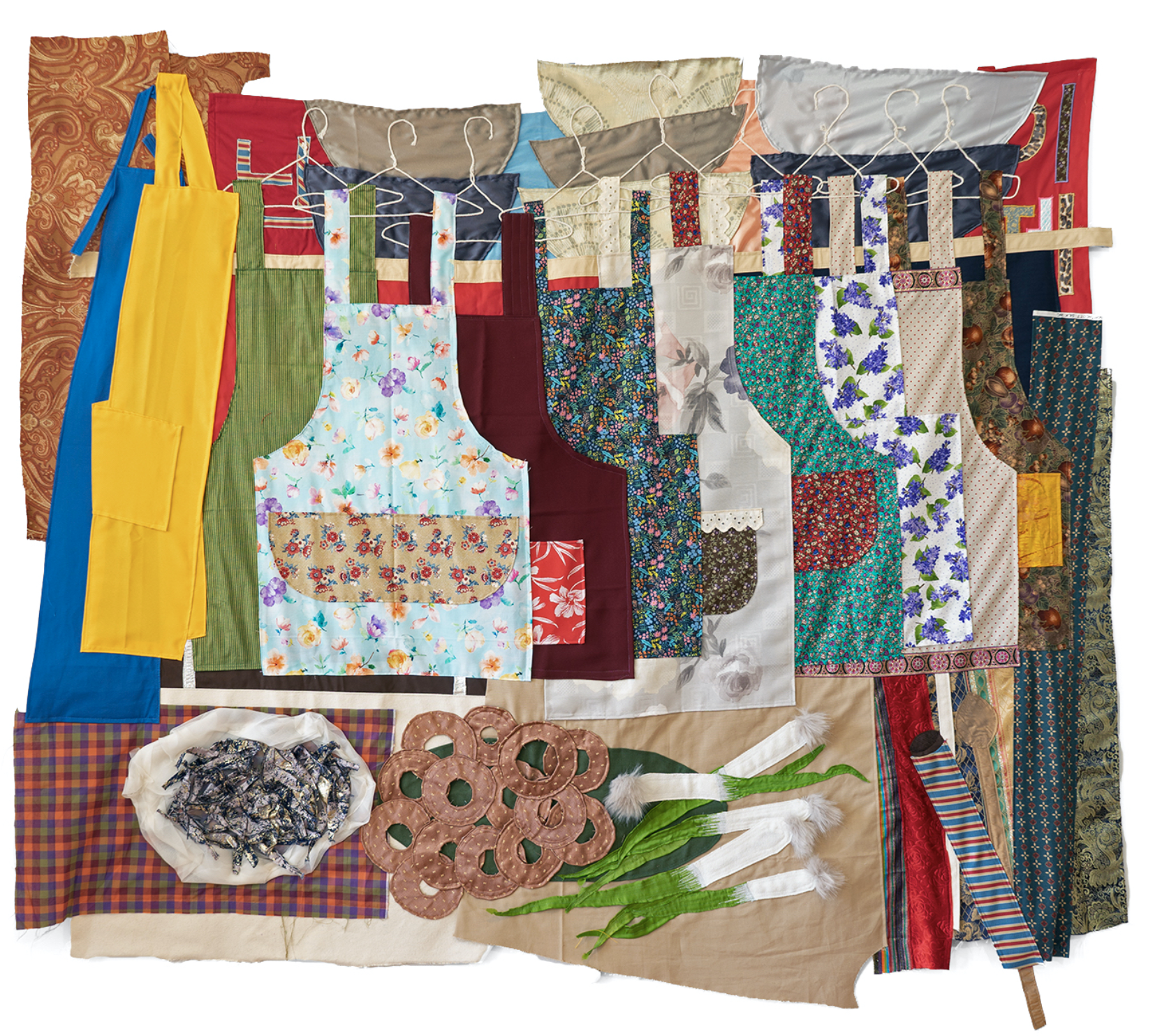 A quilt made of various fabrics depicts a rack of clothing on hangers. At the bottom of the quilt, there is a pile of spring onions, some brown circles, and a plate of grey scraps.