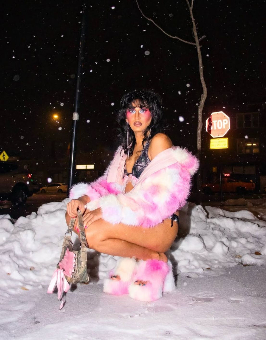 A drag queen in a furry pink coat poses in the snow