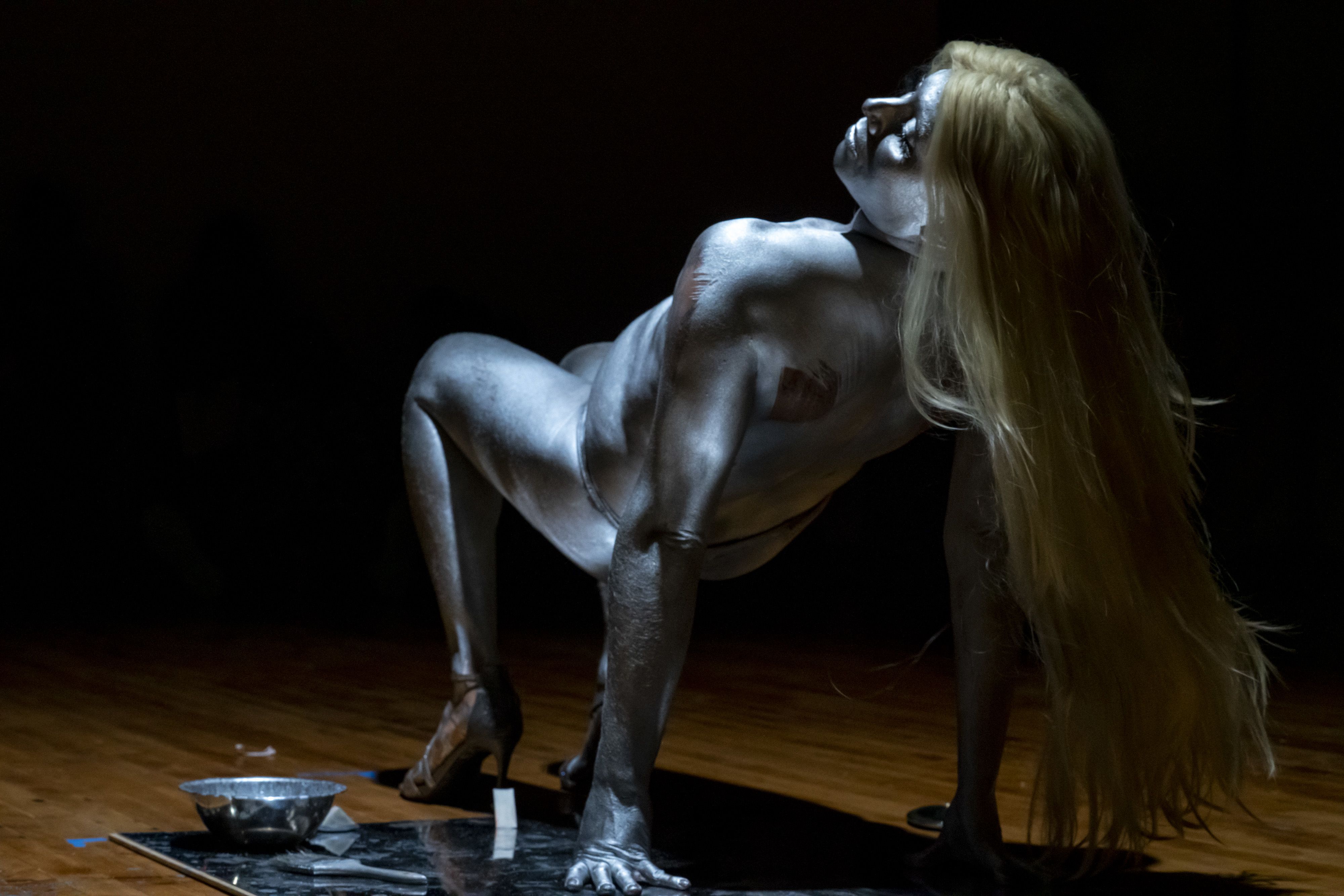 A performer painted entirely silver wearing a long blonde wig. 