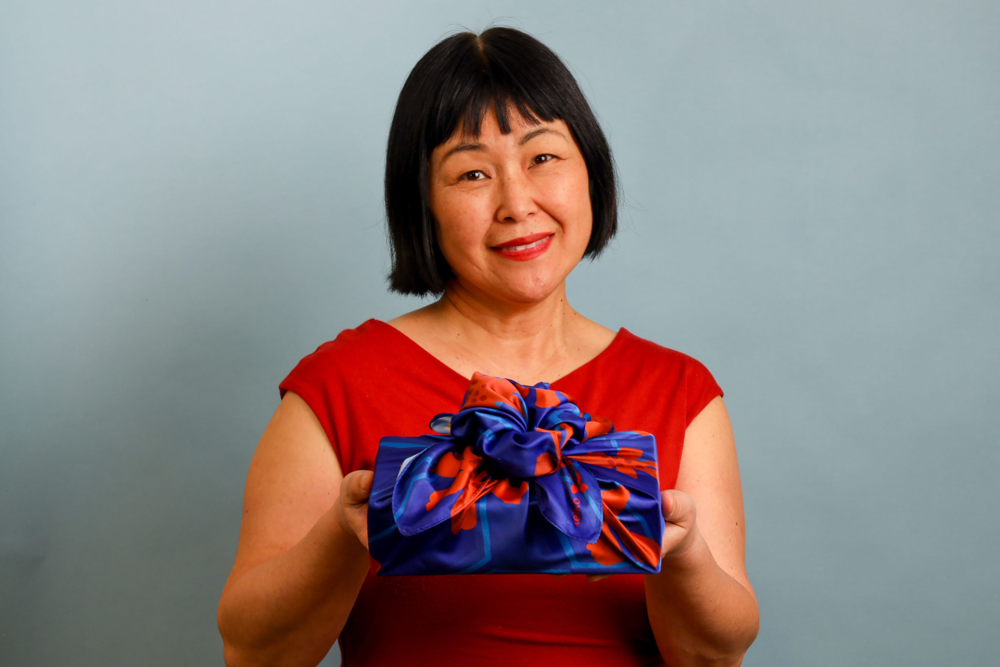 A woman holds a box wrapped in brightly colored fabric 