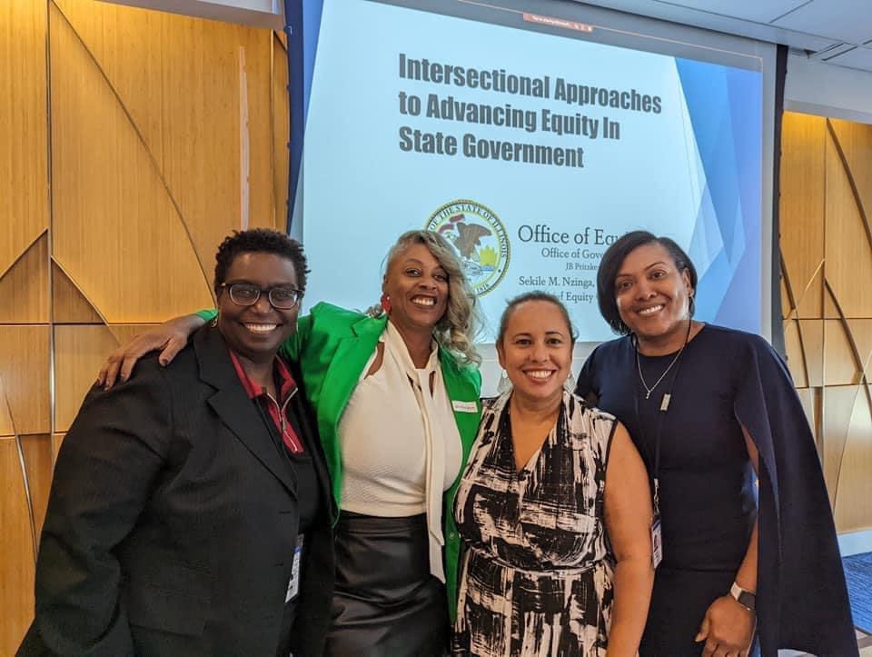 Four individuals stand in front of a presentation slide about intersectional approaches to advancing equity