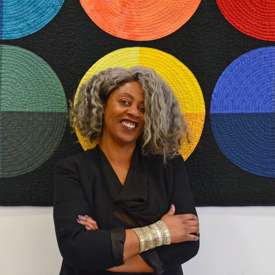 A woman stands in front of colorful fiber art