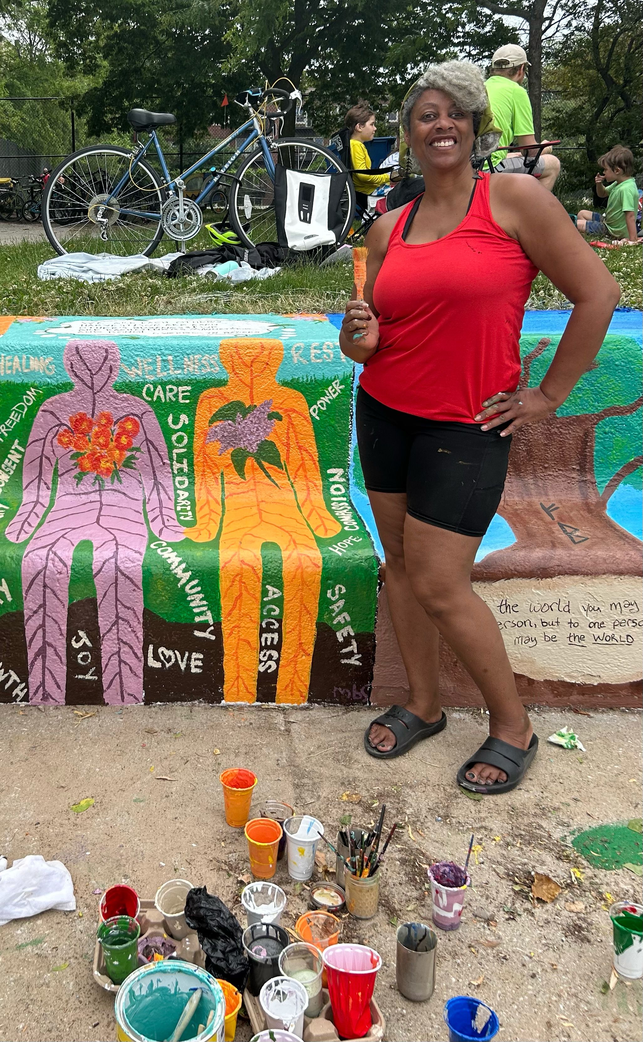 A woman with a paintbrush stands in front of a mural