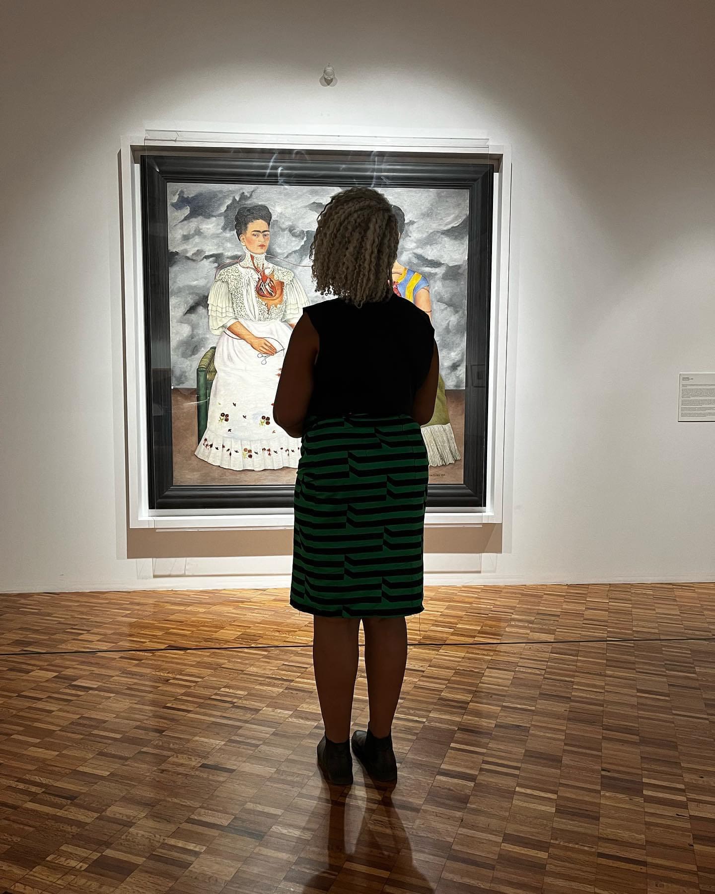 A woman stands in front of a Frida Kahlo paintingt