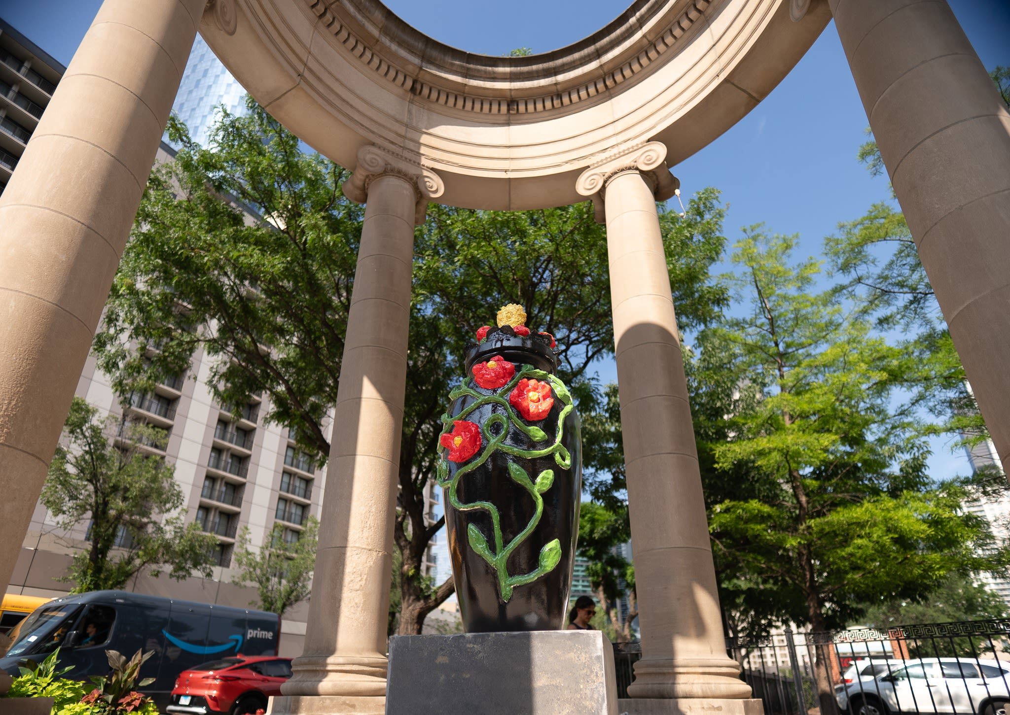 A sculpture of a black urn with red flowers and vines in an outdoor park
