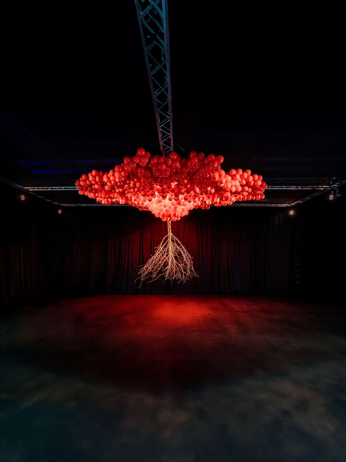 A tree made of red balloons in a dark gallery space