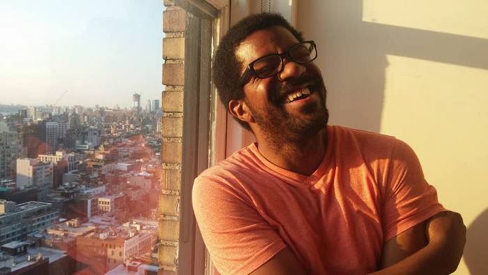 A photo of a man in glasses laughing by a window