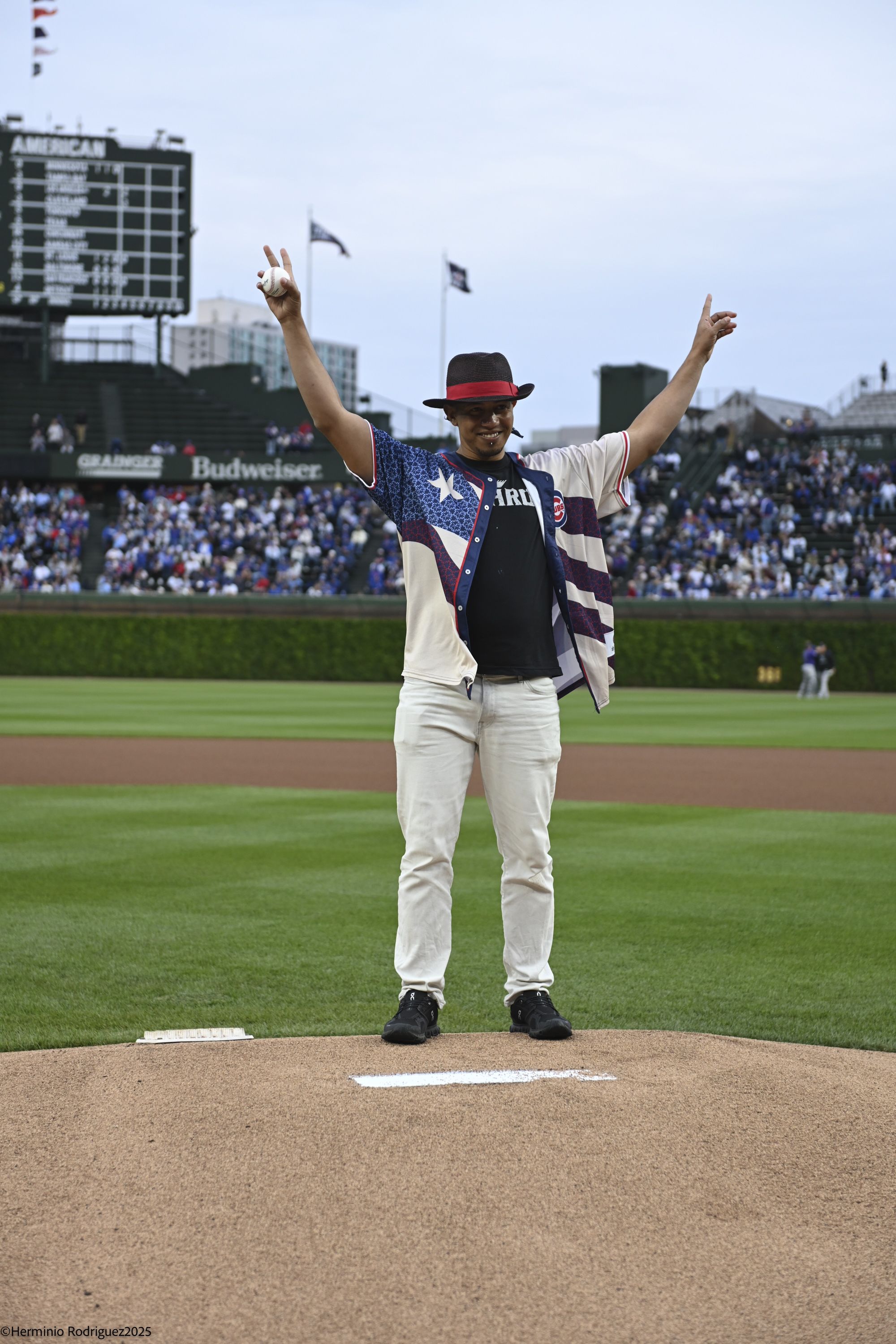 A man stands on the pitching mound at Wrigley Field with his arms in the air