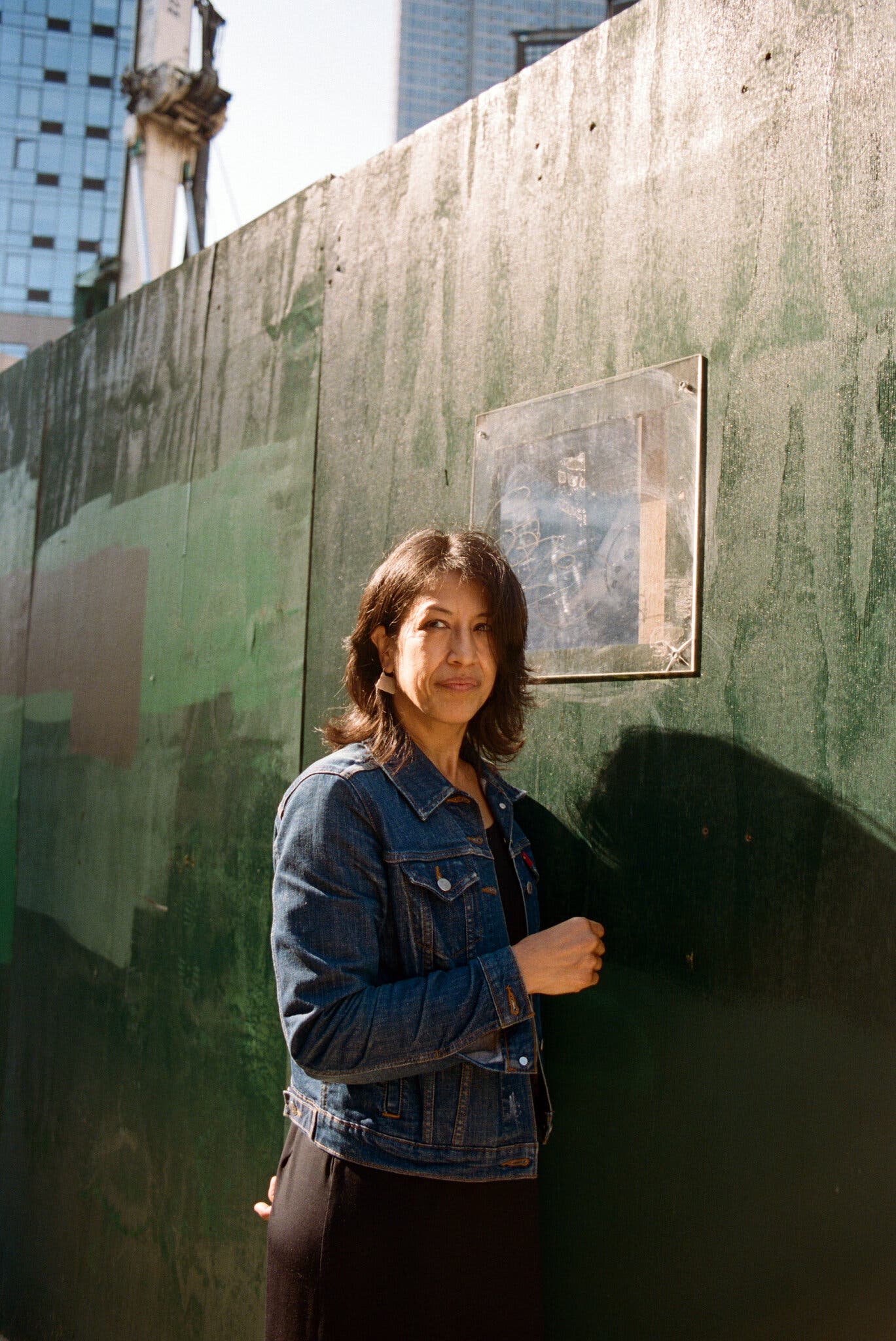 A woman stands against a green wall