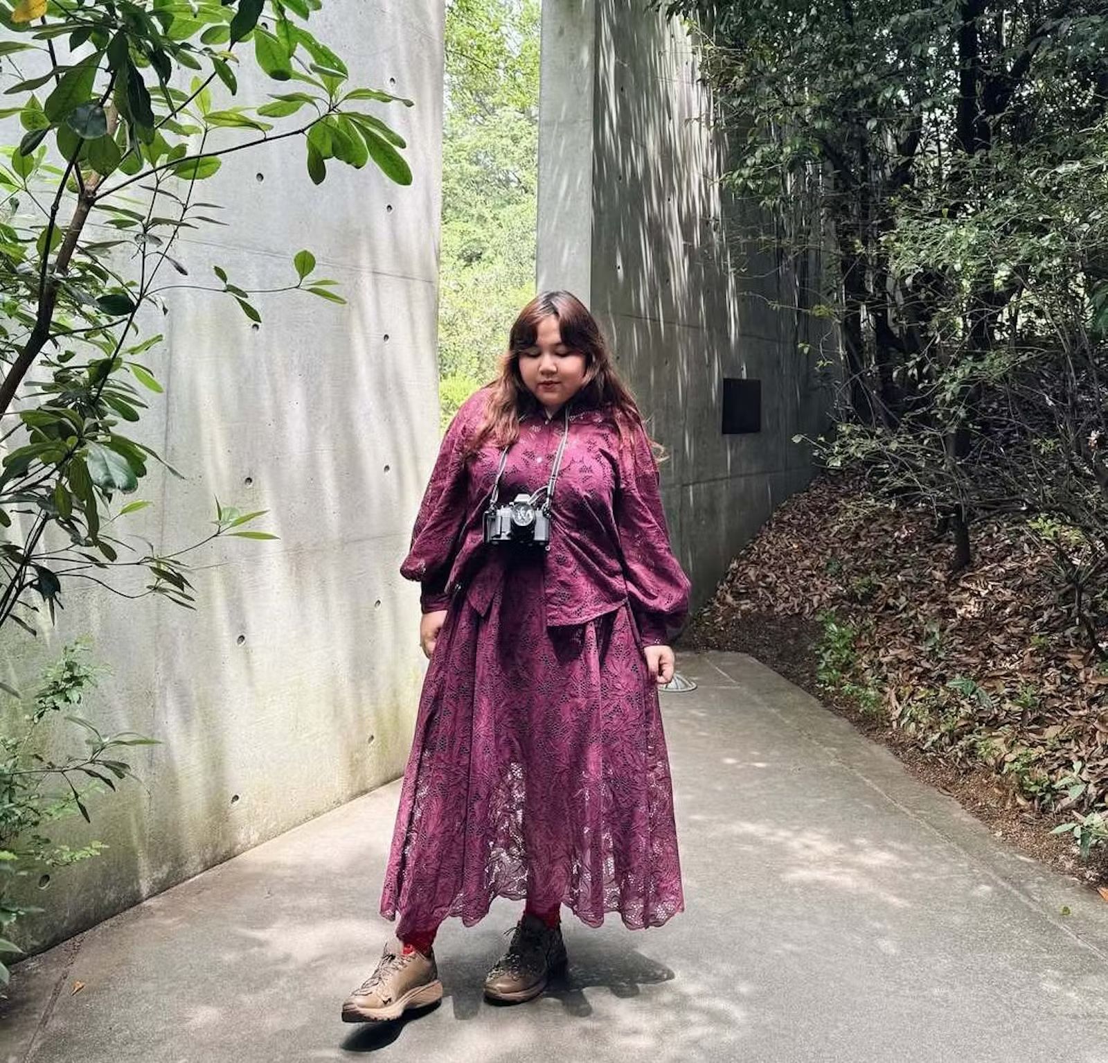 A woman in a garden wears a maroon lace set