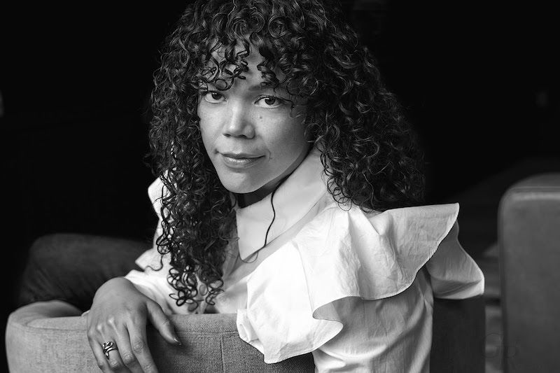A black and white photo of a woman with curly hair in a white shirt