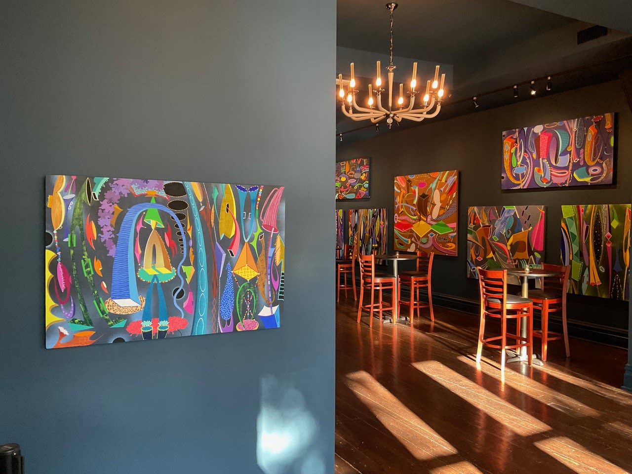Several bright abstract paintings in a space with a chandelier