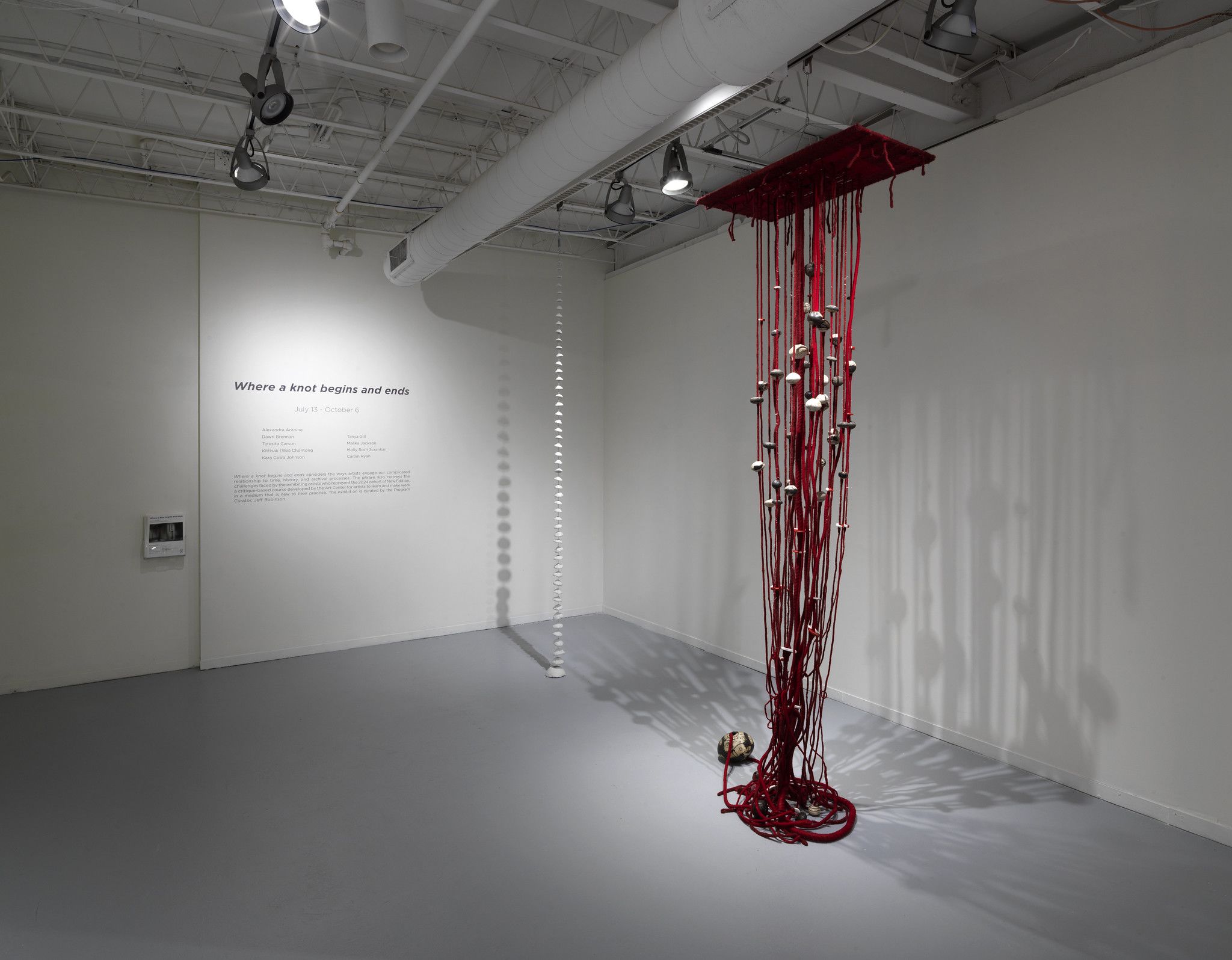 A gallery installation with red threads hanging from a ceiling
