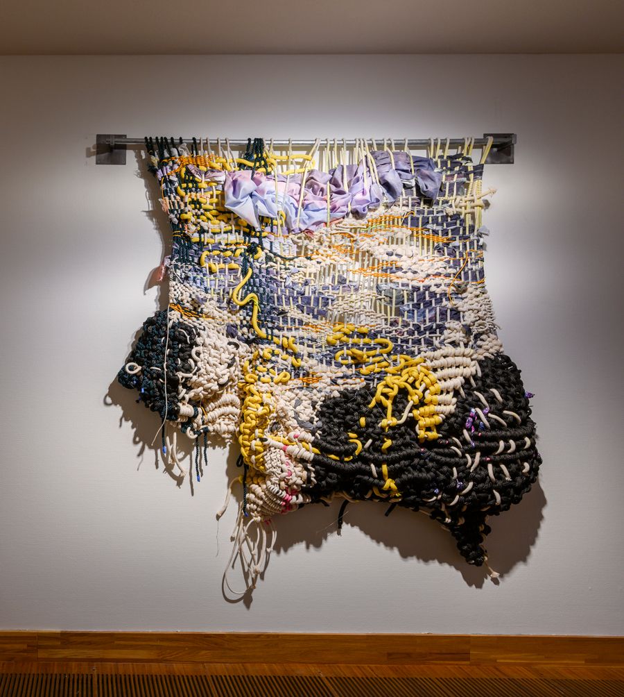 A large woven structure hangs on a white wall