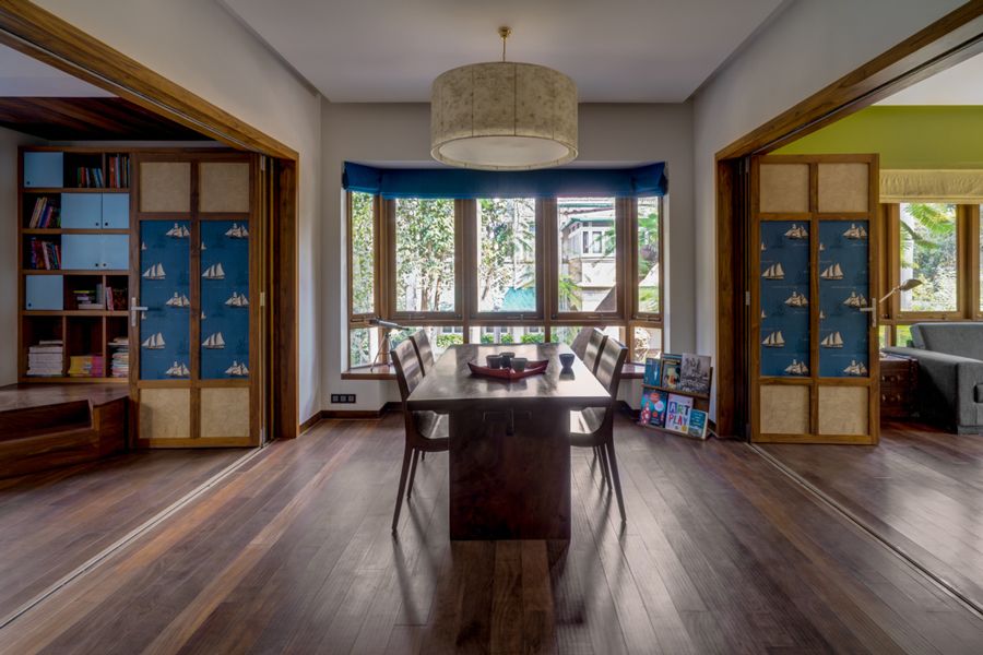 Photo of a dinging room table and two chairs in a large, open room in front of a large window with a cylindrical light fixture hanging above