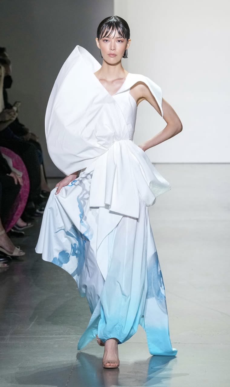 An image of a model on a runway. The model is wearing a white and blue gown designed by Michelle Sumin Suh.
