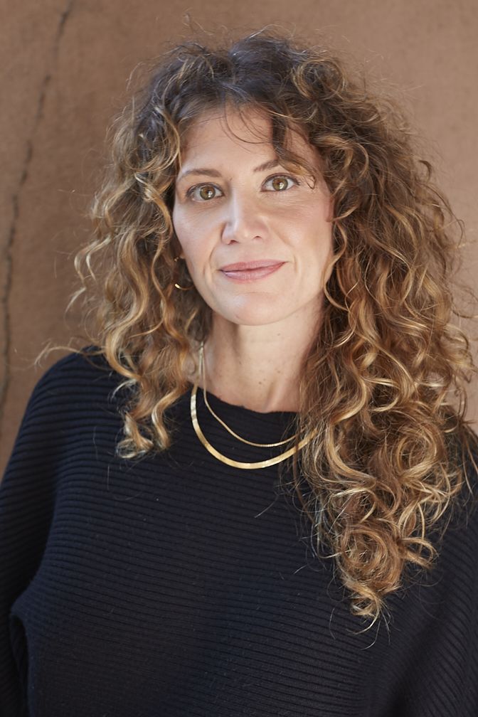 A portrait of an artist with curly hair and gold necklaces