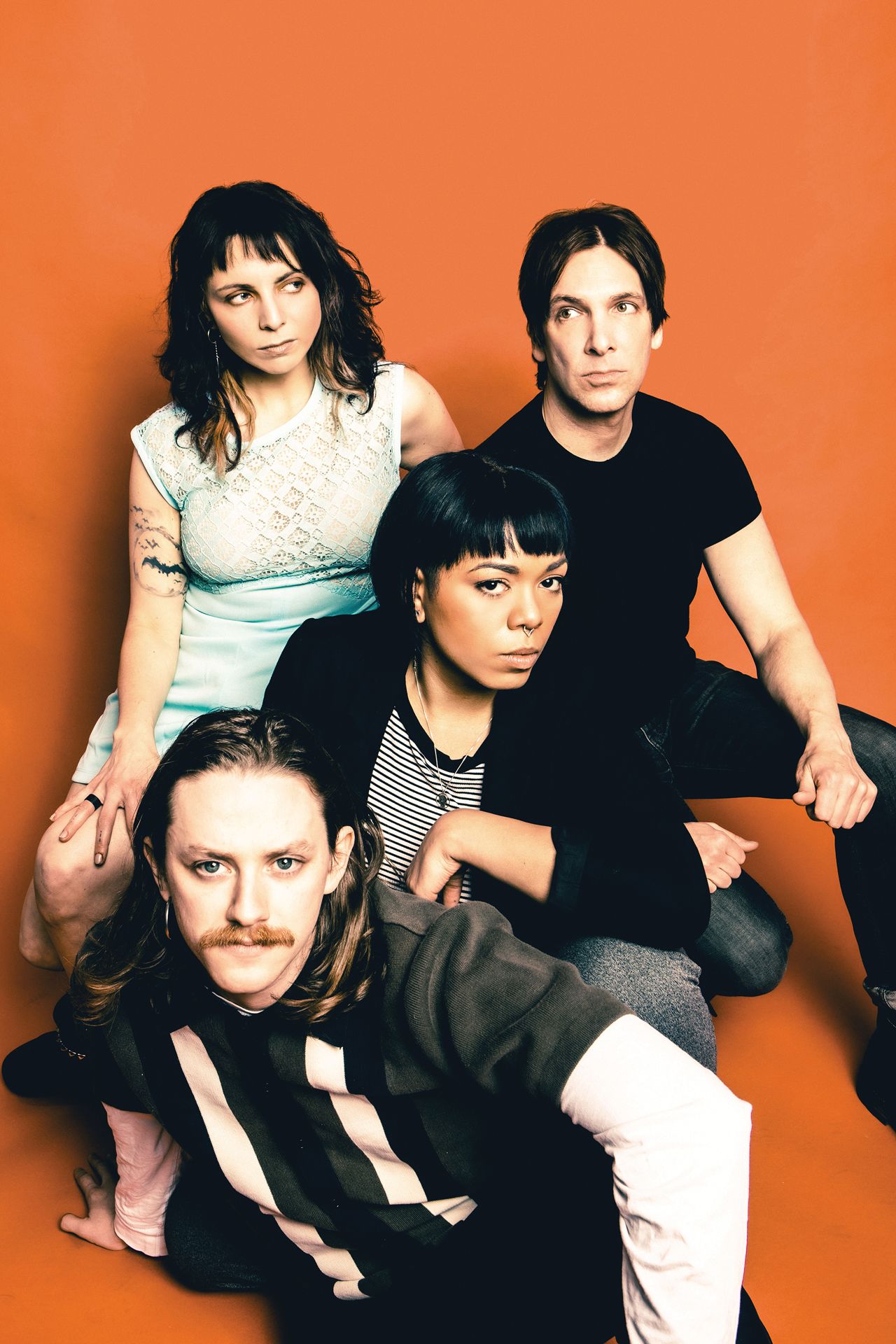 A band portrait of four musicians posing in front of an orange background