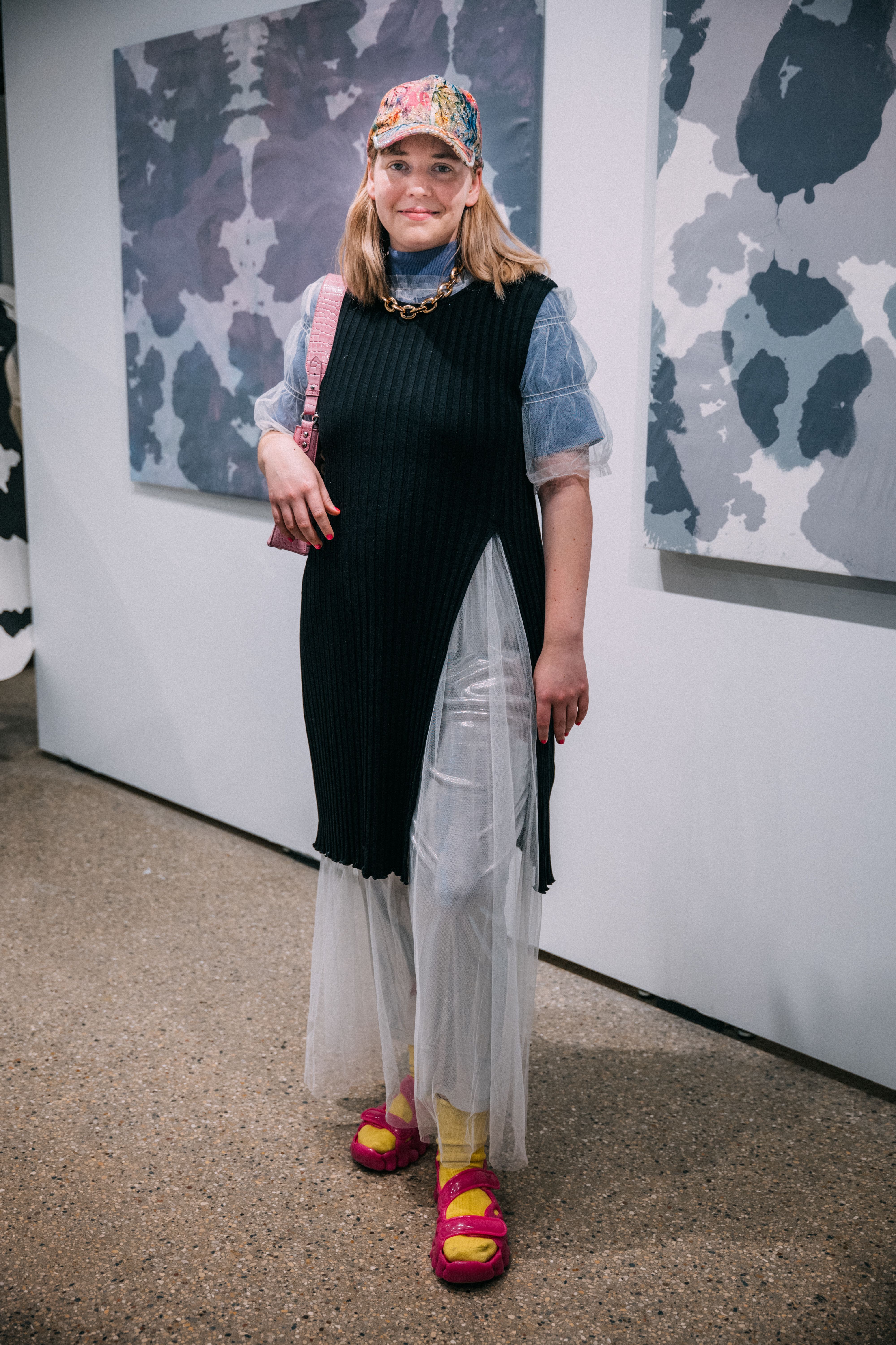 A student poses in front of two canvases while wearing a layered outfit.