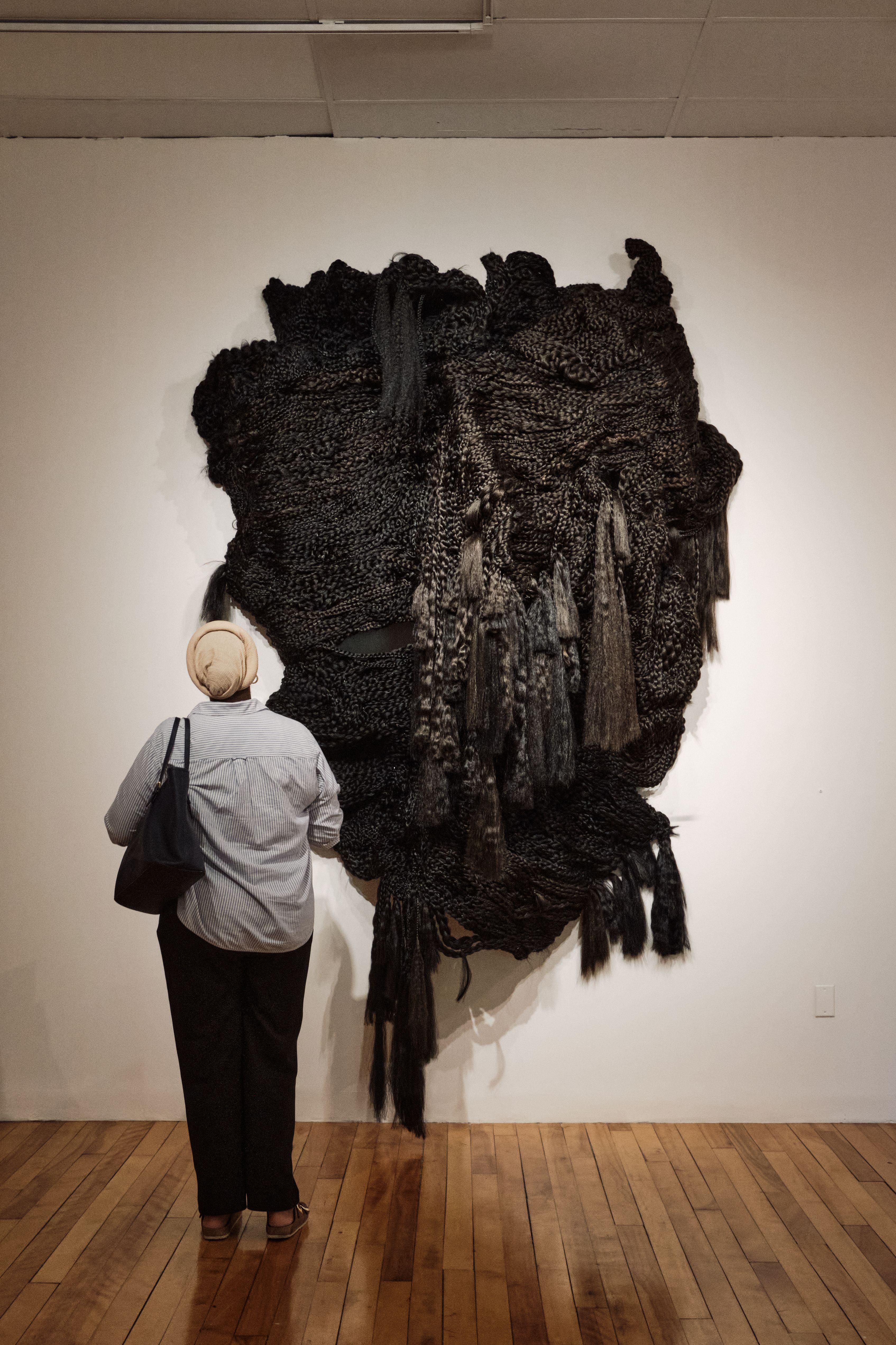 A person stands in front of a black fiber art installation