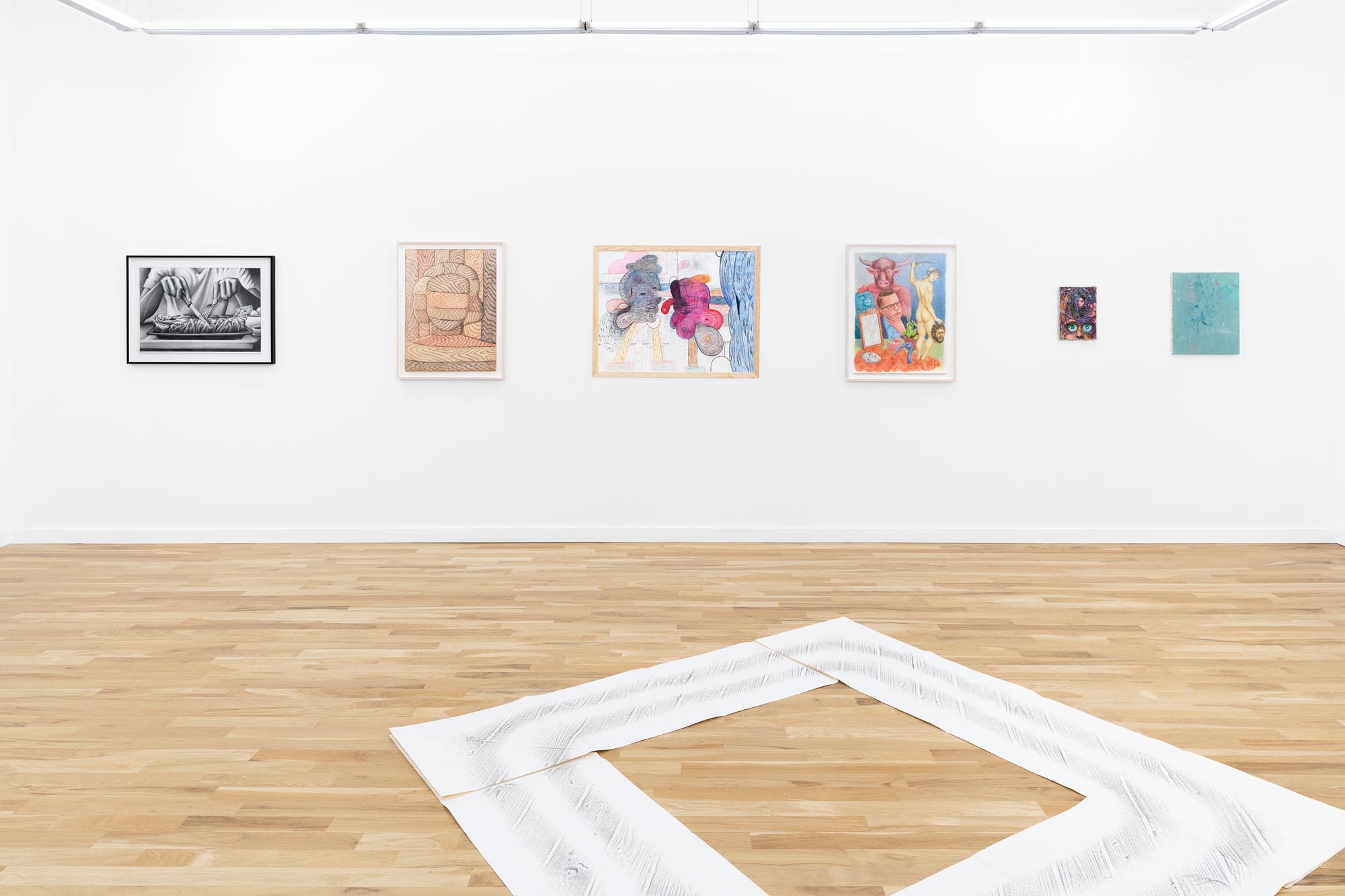 A wood floored, white-walled gallery with art mounted on the walls
