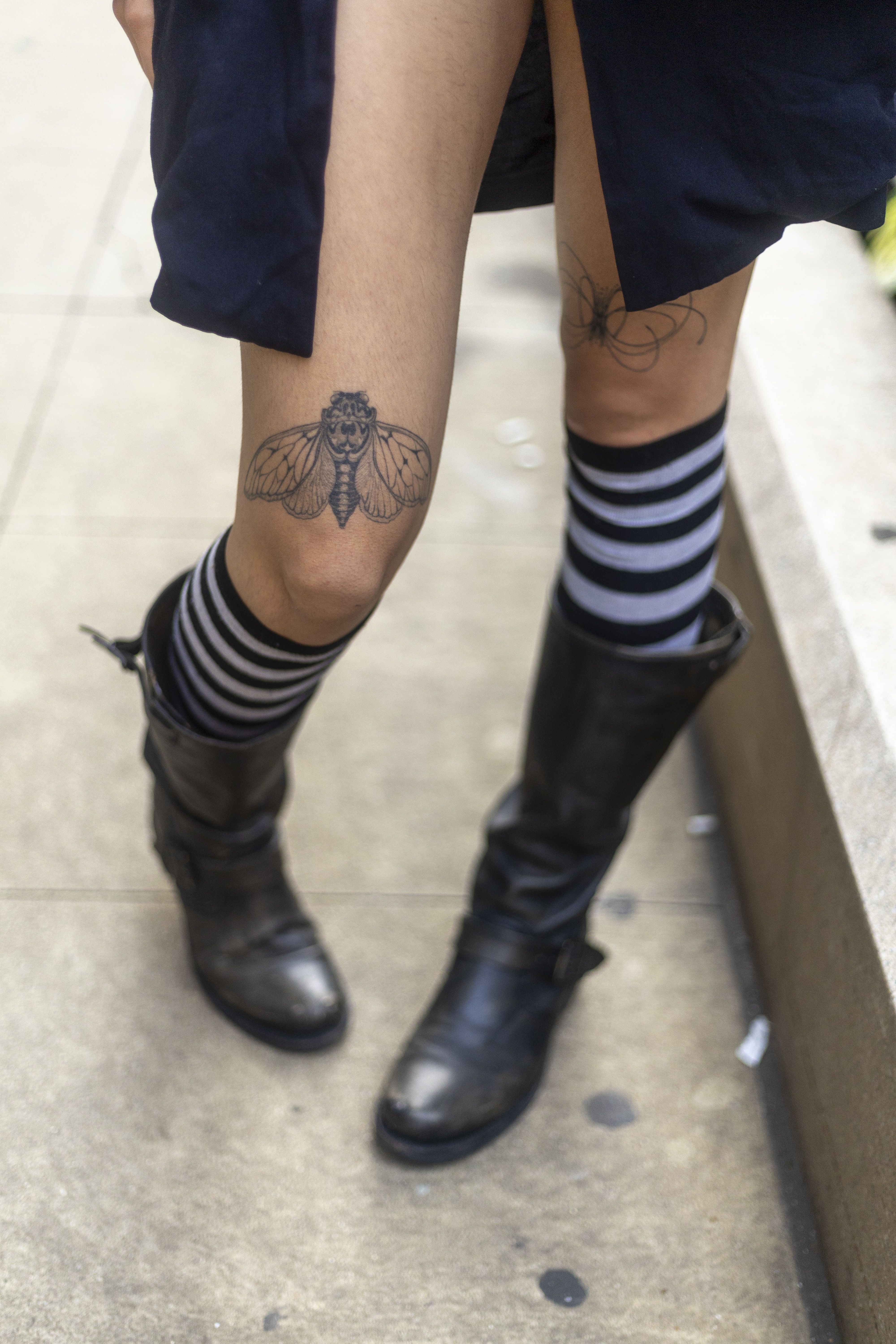 A photo legs in striped socks and boots with a tattoo of an insect above the knee