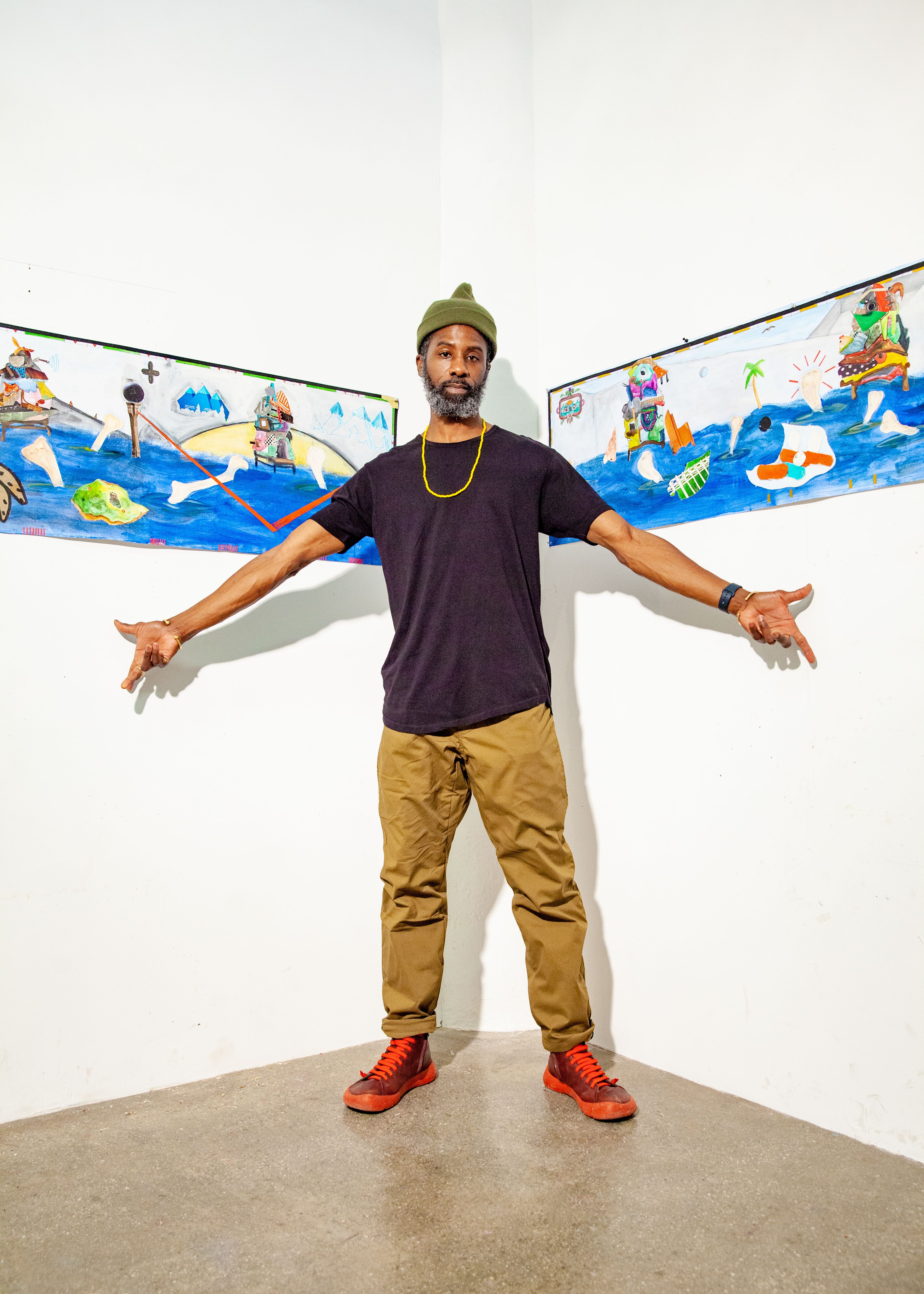 An artists poses in front of two works of art on white walls