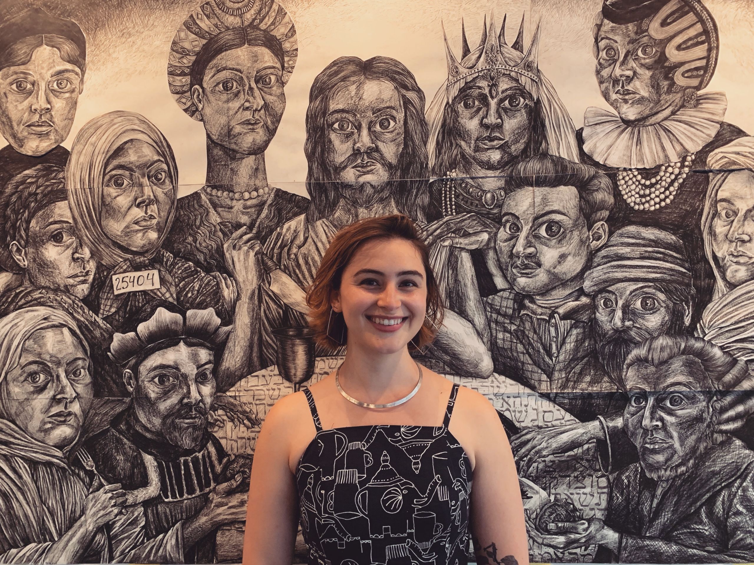 A young woman stands in front of a black-and-white drawing of figures