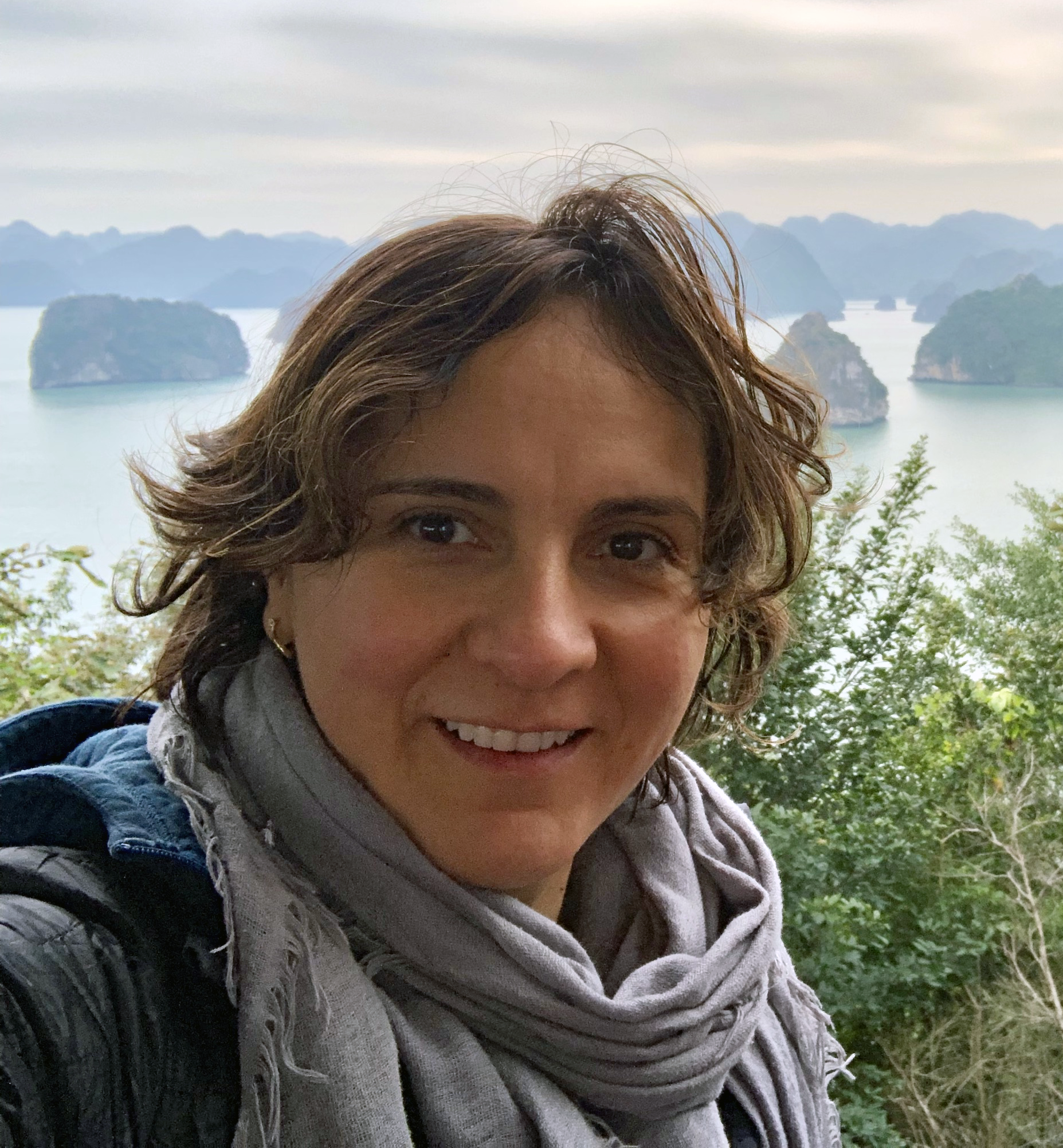 A woman poses in front of a beautiful scene of mountains and water