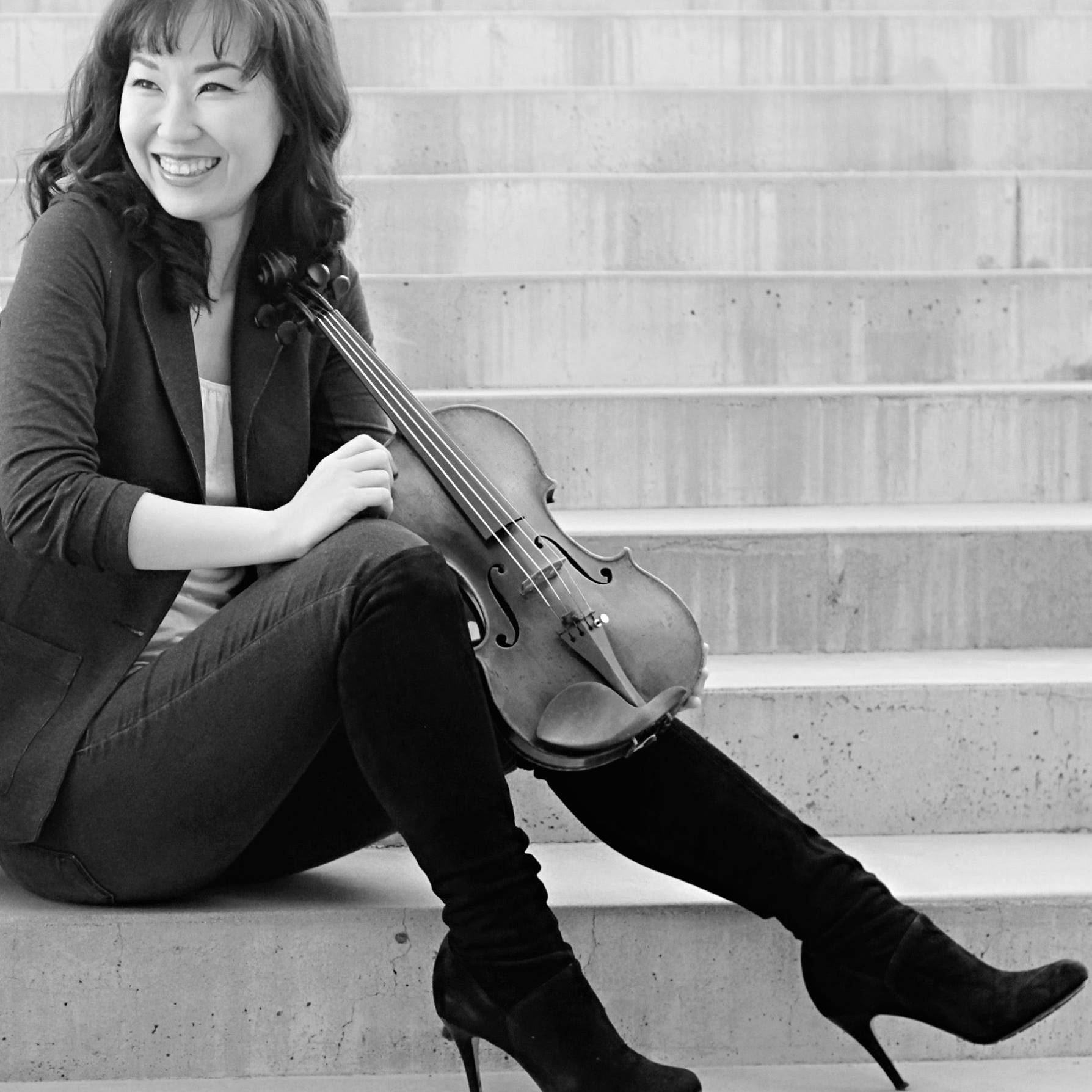 A young woman sits on stairs holding a violin