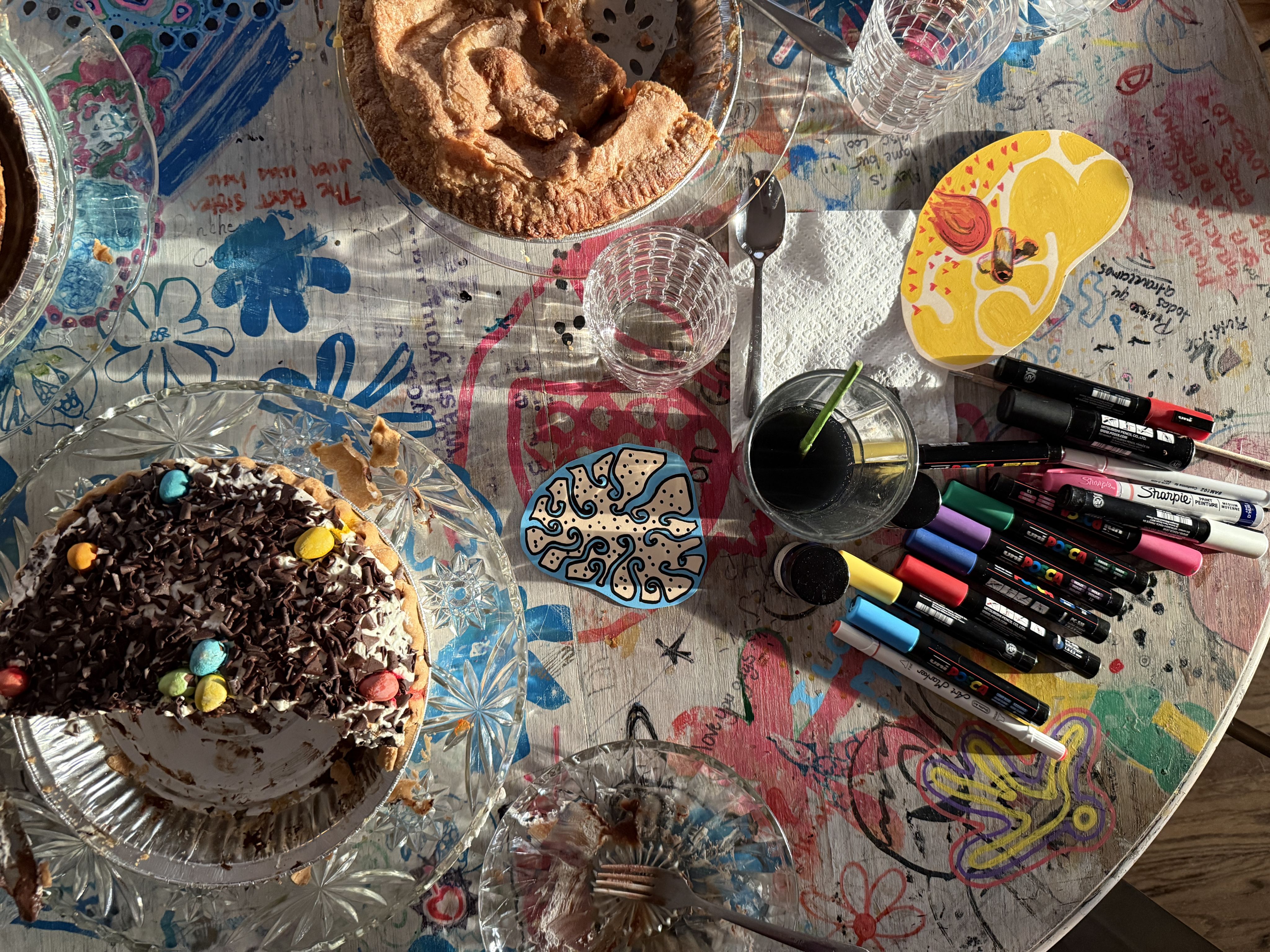 A table scattered with art supplies and pies in tins. 