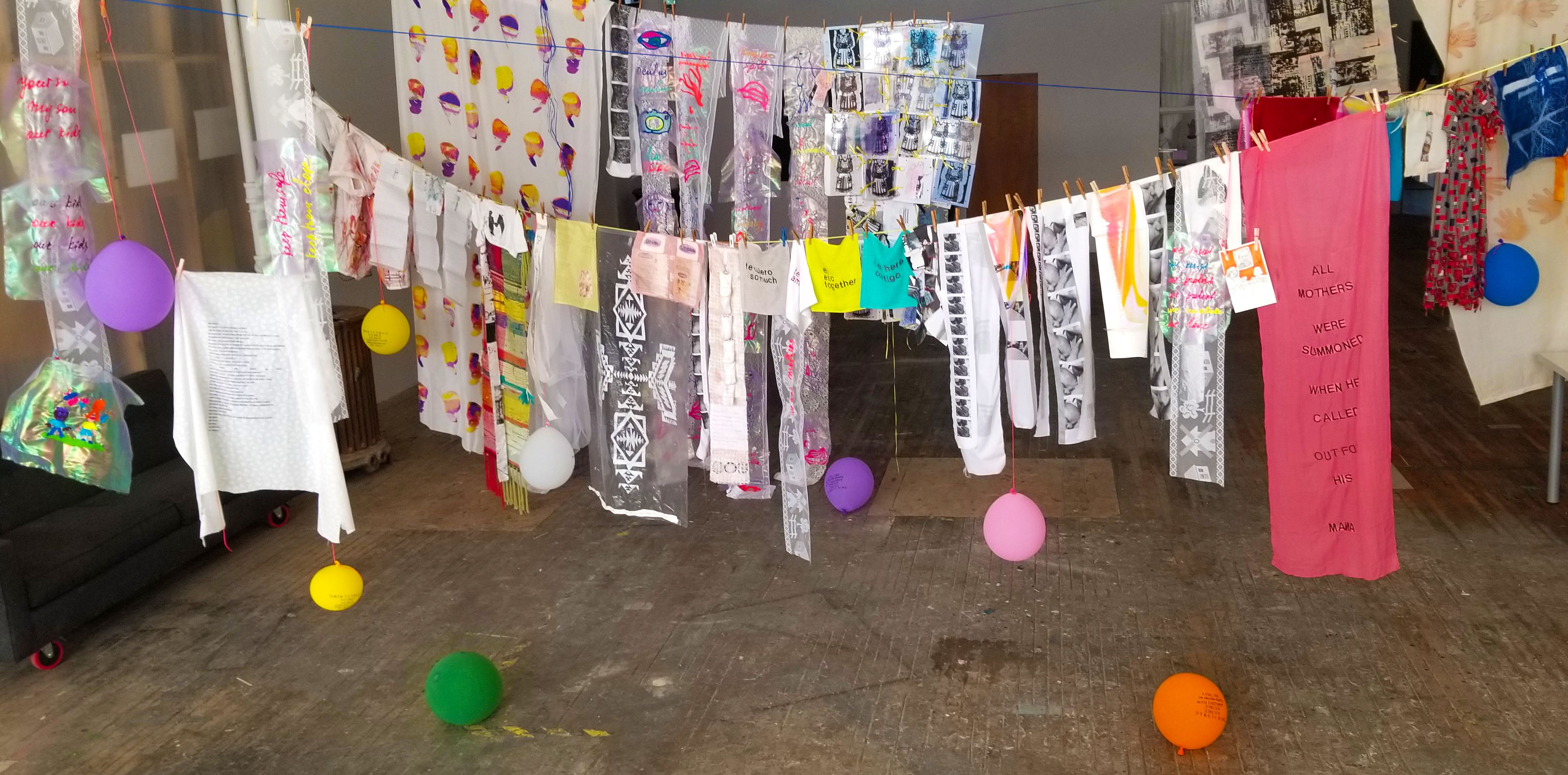 Artwork and balloons strung along a clothesline in a gallery space.