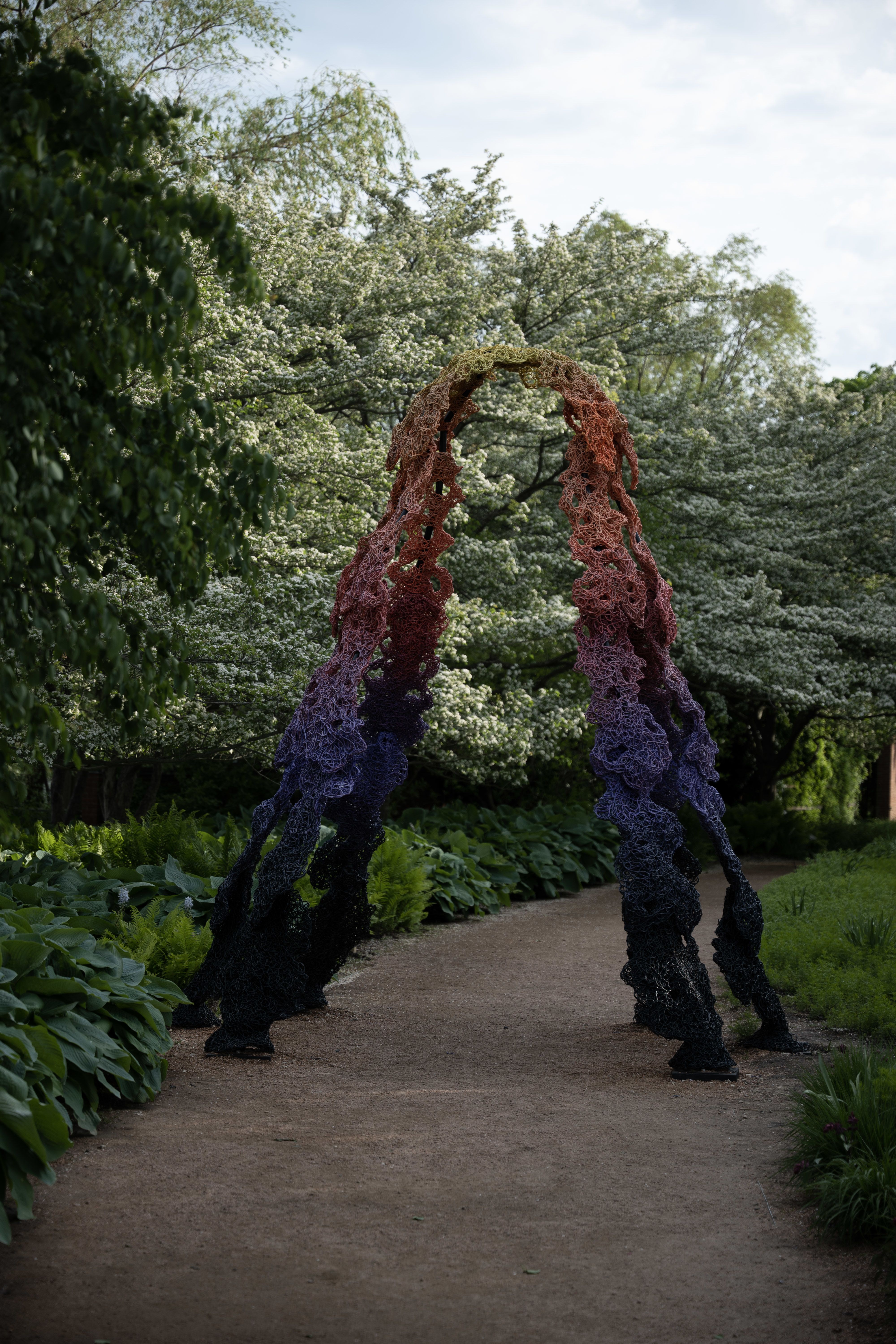 An colorful, organically shaped archway along a dirt path. Trees and plants are along the path.