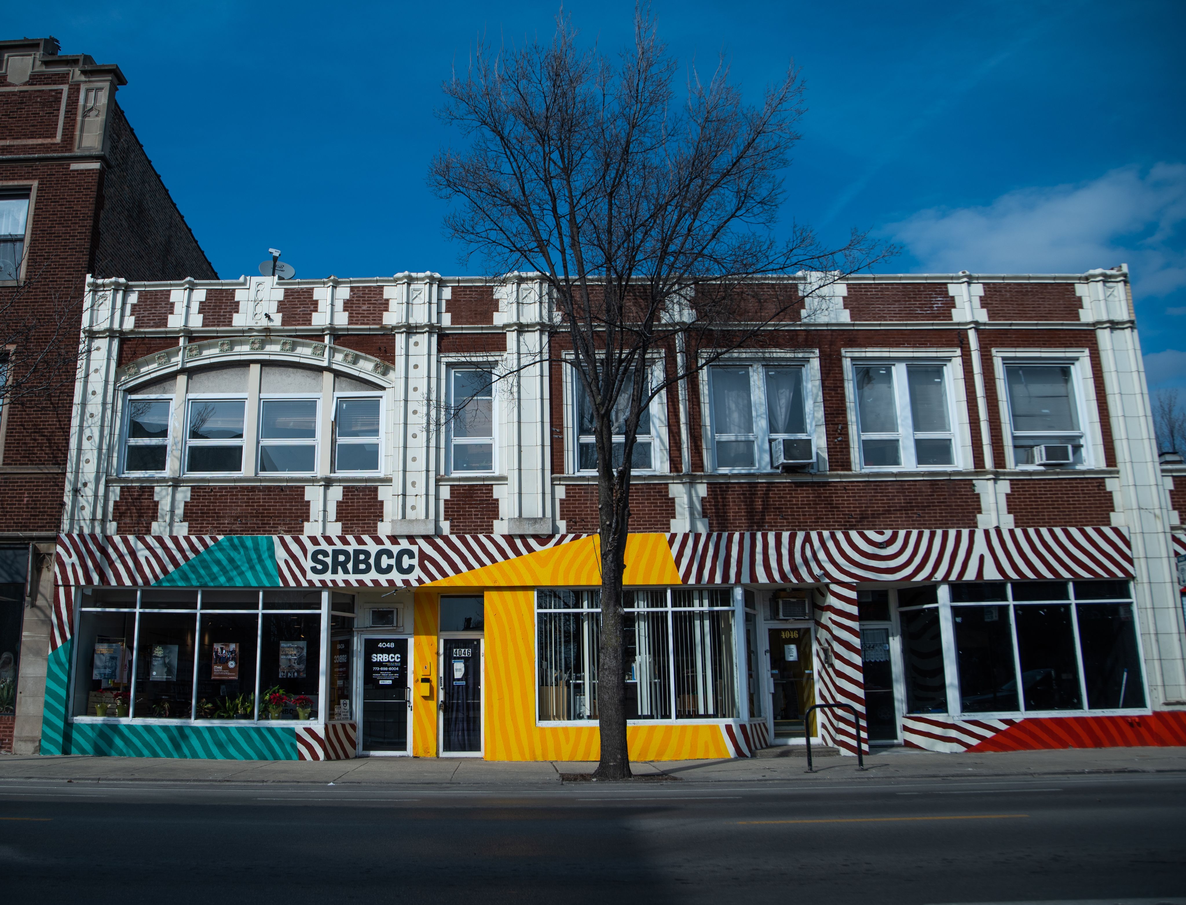 A photo of the exterior or a two-story brick cultural center brightly painted with circles of black, teal, and yellow paint