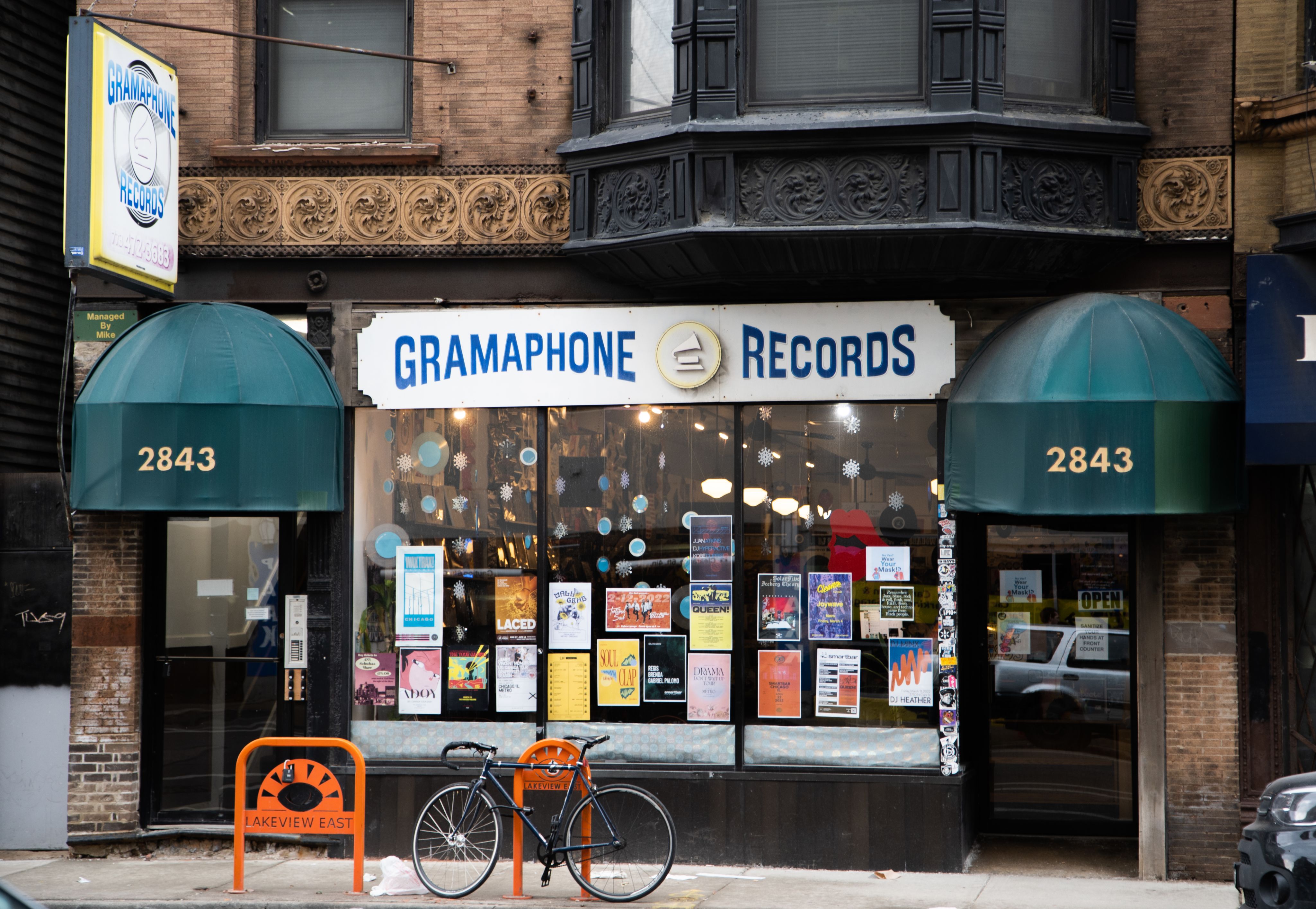 The exterior of a record shop with posters in the window, green awnings to the side, and a bike parked out front