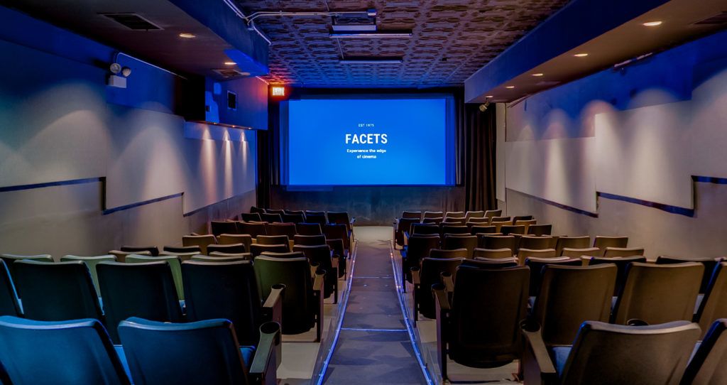 An interior of a small movie theater screening room, with a blue screen reading Facets at the front of rows of seats