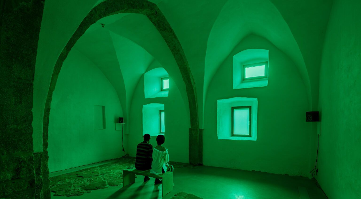 Two figures sit in a green-lit chapel space