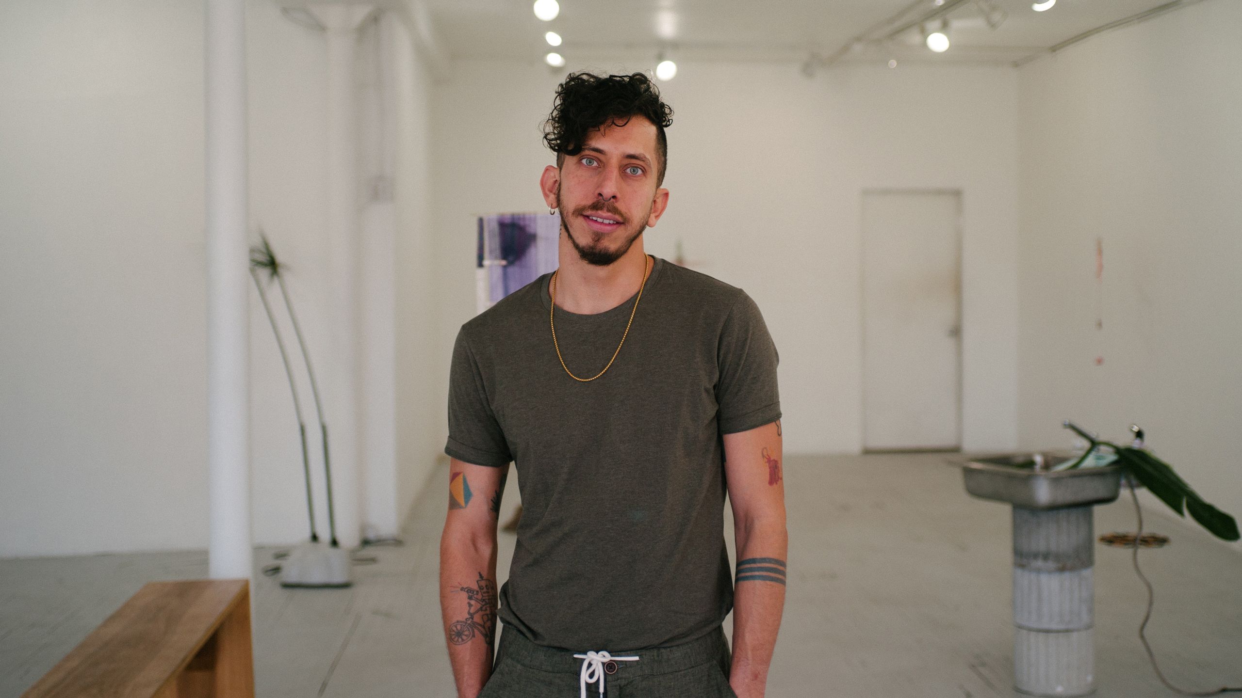 A man in a t-shirt with tattoos stands in front of a white-walled gallery space