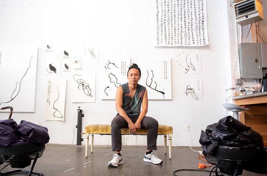 An artist sitting on a yellow bench in his white-walled studio